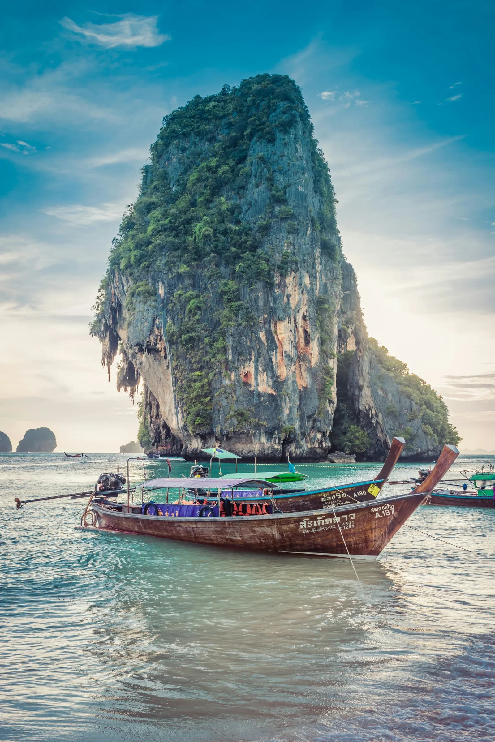 Limestone karst rising from sea with traditional Thai longtail boat in foreground