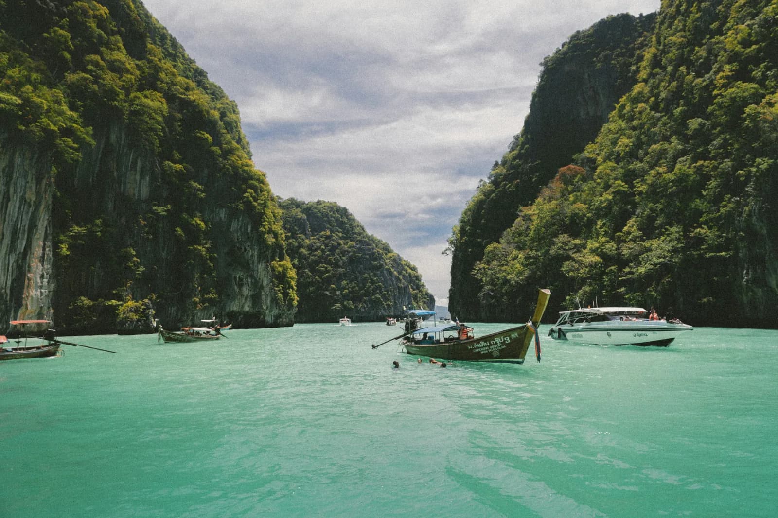 A longtail boat in turquoise water between towering limestone karst cliffs.