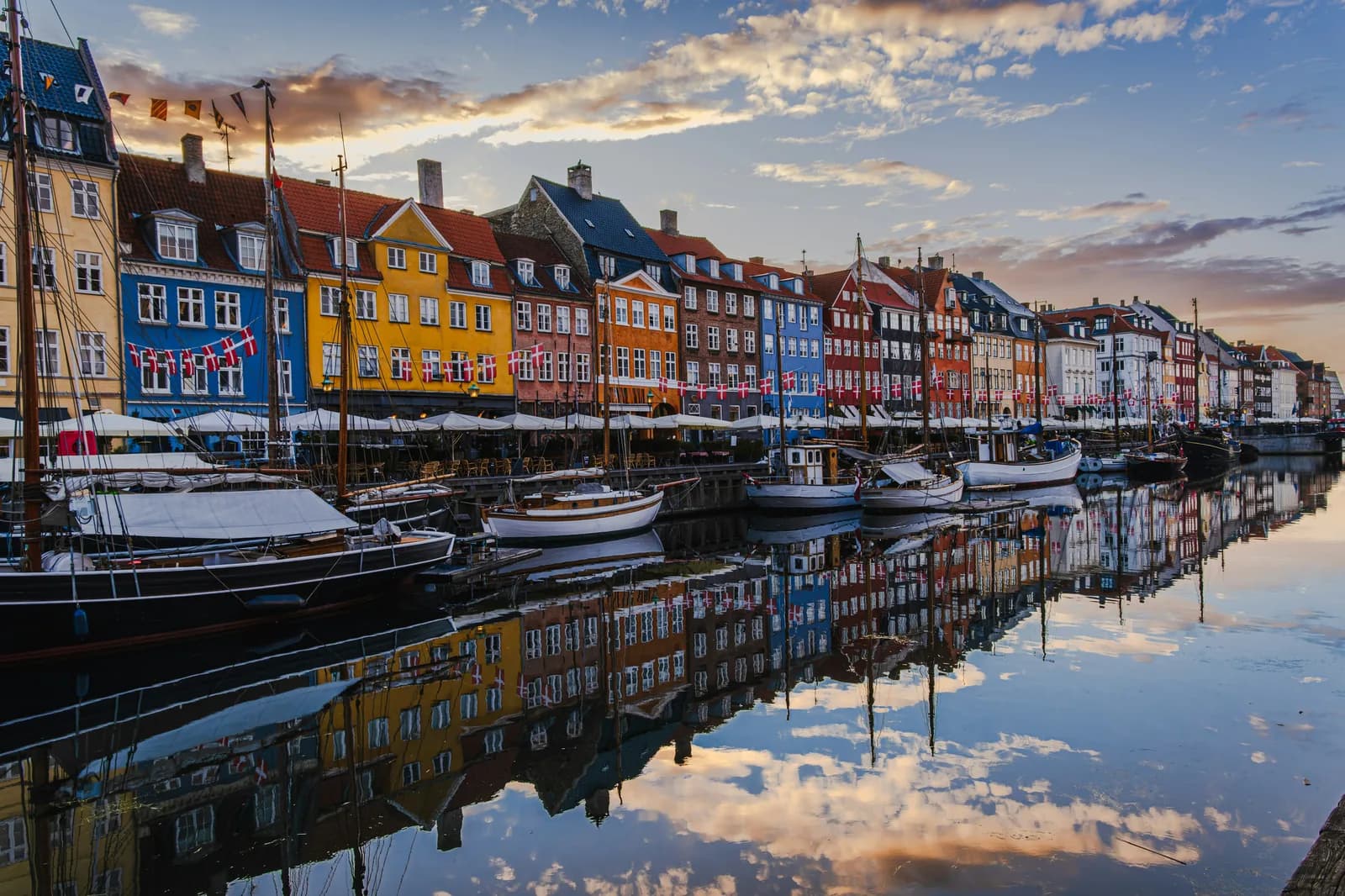 The colourful gabled townhouses and moored wooden boats along the Nyhavn canal in Copenhagen, reflected in still water.