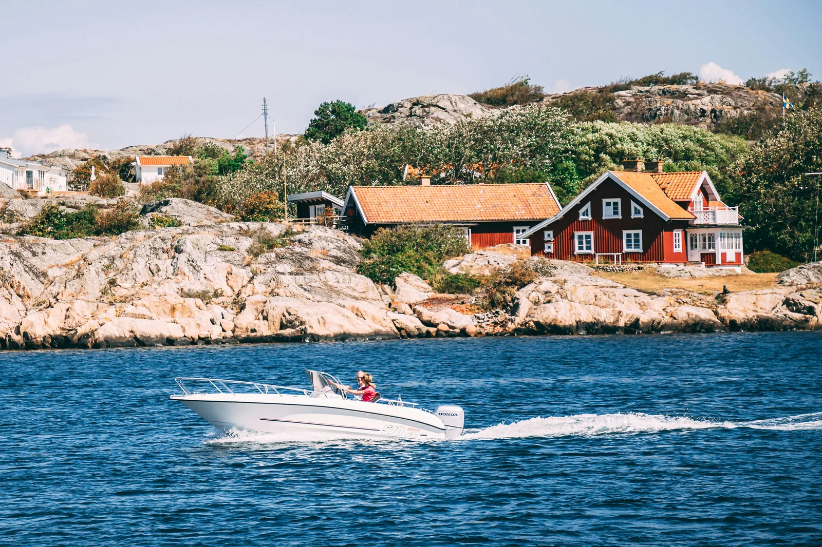 A small motorboat crossing blue water past red wooden sea cabins in the Strömstad archipelago.